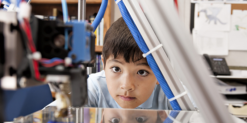 A young boy watching a 3D printing machine in progress