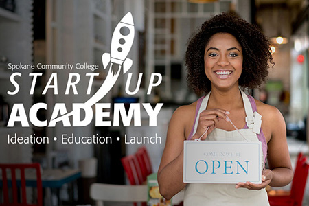 Spokane Community College Start Up Academy - African American woman standing in a cafe with an apron on holding an open sign